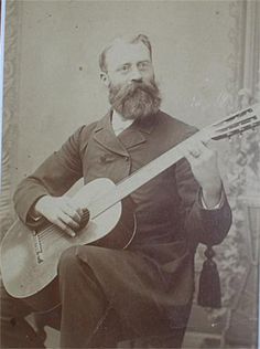 an old black and white photo of a man with a beard holding a guitar in his right hand