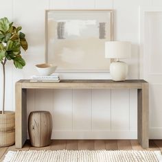 a wooden table with a vase on top and a plant next to it in front of a white wall