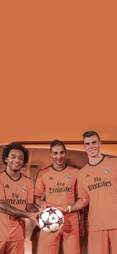 three men in orange soccer uniforms holding a ball