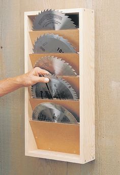 a person holding a circular saw in front of a wall mounted tool holder with six circular blades