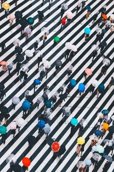 many people are walking across the crosswalk with their umbrellas up in the air