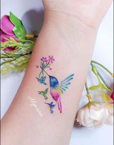 a small tattoo on the wrist of a woman with flowers and birds around her arm