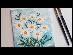 two paintbrushes sitting next to a painting of daisies