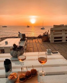 two glasses of wine are sitting on a table with food and drinks in front of the ocean