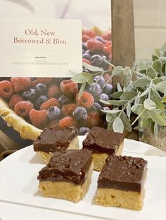 three pieces of cake sitting on top of a white plate next to a basket of berries