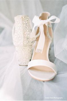 a pair of white high heel shoes sitting on top of a bed next to a bride's veil