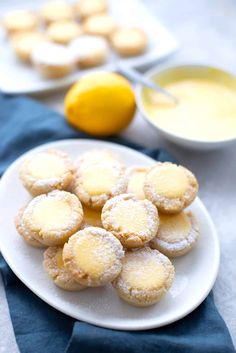 lemon cookies on a white plate next to a bowl of orange juice and a blue towel