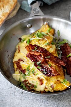 a metal bowl filled with bacon and cheese on top of a table next to bread