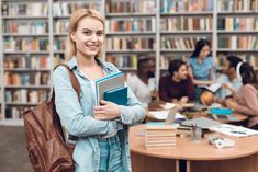 a woman holding a book in front of a library full of people sitting at tables