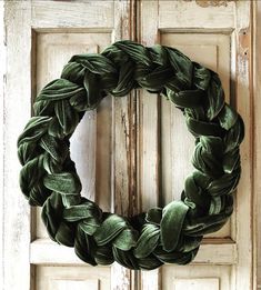 a green wreath hanging on the front door of an old wooden door with peeling paint