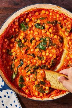 a person is dipping some bread into a pot of stew with spinach and chickpeas