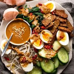 a white plate topped with meat and veggies next to an egg shell on top of noodles