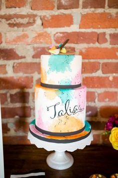 a colorful cake sitting on top of a table next to a brick wall and flowers