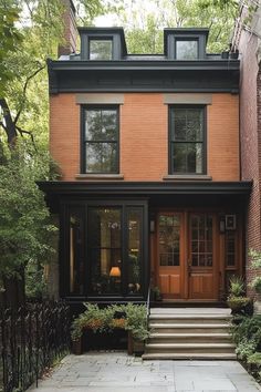 a brick house with black trim and two story windows on the second floor is surrounded by greenery