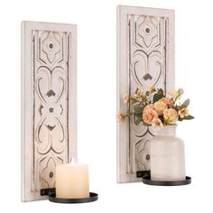 two white wall sconces with flowers on them and a candle in the middle