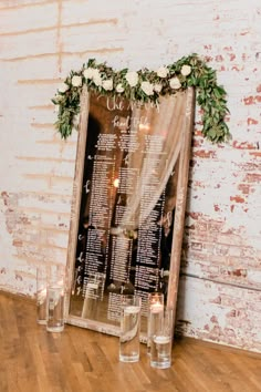 a wedding seating chart with flowers and greenery is displayed in front of candles on the floor