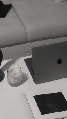 an apple laptop computer sitting on top of a white table next to a glass cup