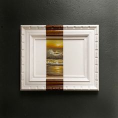 a white frame hanging on the wall with a brown and white painting in front of it