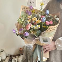 a woman holding a bouquet of flowers in front of a white wall with pictures on it