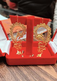 two pairs of gold earrings are in a red display case on a wooden table with other jewelry items