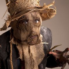 an old scarecrow wearing a straw hat and holding a dead bird in his hand