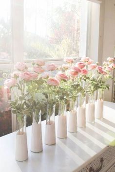 several white vases with pink flowers in them on a table next to a window