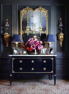 a table with flowers on it in front of a mirror and two gold sconces