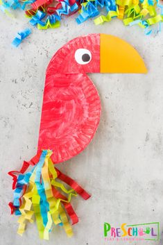 a paper plate bird with colorful streamers around it's neck and beak, sitting on top of a cement surface