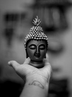 a small buddha statue sitting on top of a person's hand in black and white