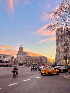 cars and motorcycles are driving down the street in front of some tall buildings at sunset