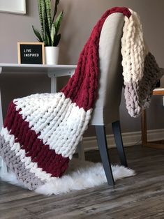 a chair with a knitted blanket on top of it next to a table and potted plant