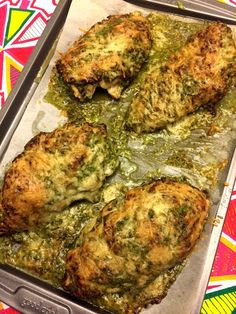 four pieces of chicken covered in pesto and cheese on a baking sheet with colorful background