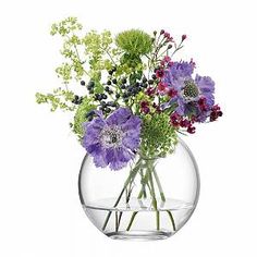 a clear vase filled with purple flowers and greenery on top of a white background