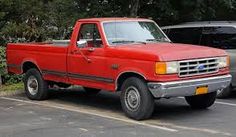 a red pick up truck parked in a parking lot next to other cars and trees