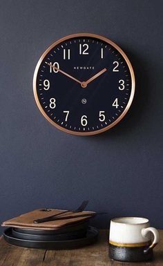 a black and gold clock on a wall next to a coffee cup with a laptop