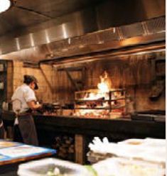 two men working in a restaurant kitchen with flames coming out of the oven and food on the counter