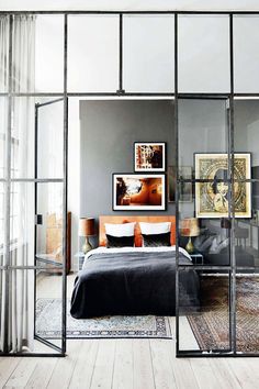 a bedroom with glass walls and a bed in the middle, surrounded by wooden floors