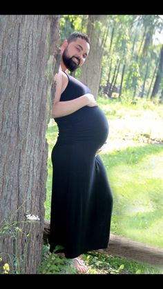 a pregnant woman standing next to a tree