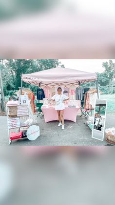 a woman standing in front of a pink tent with pictures on it and other items