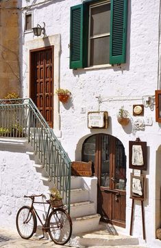 a woman sitting on the steps in front of a white building with green shutters