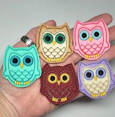 four handmade owl magnets in different colors and sizes on a person's palm