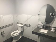 a white toilet sitting next to a sink in a bathroom under a mirror and towel dispenser