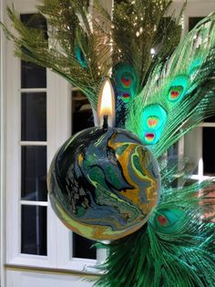 a candle is lit in front of a peacock ornament with feathers on it