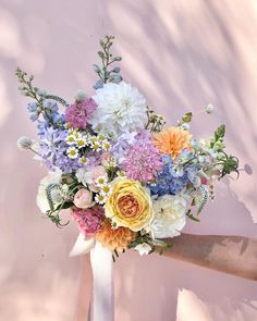 a bouquet of flowers is being held by someone's hand in front of a pink wall