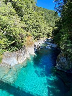 the water is crystal blue and clear in this river that runs between two mountains with trees on both sides