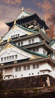 a large white and gold building sitting on top of a lush green hillside under a cloudy sky