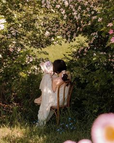 a woman sitting on top of a wooden chair next to a lush green forest filled with pink flowers