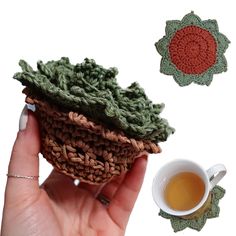 a hand holding a small crocheted basket next to a cup of tea and coaster