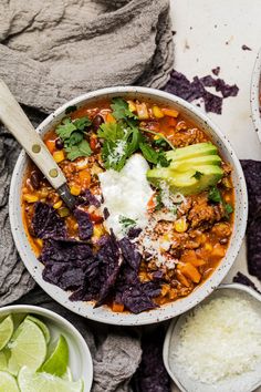 two bowls filled with chili, tortilla chips and avocado garnished with sour cream