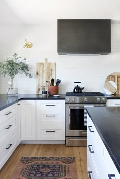 a kitchen with white cabinets and black counter tops, an area rug and potted plant